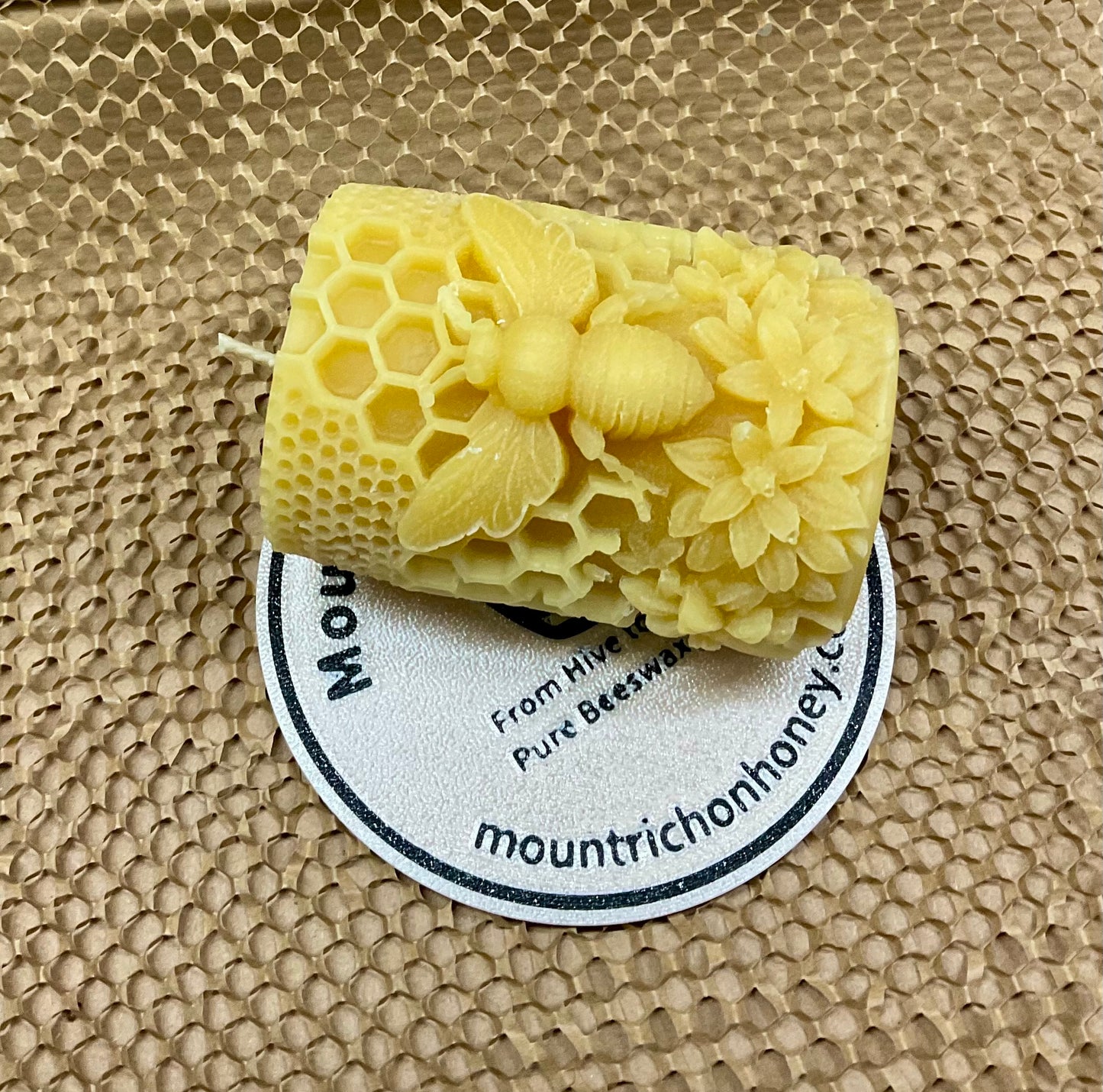 Beeswax candle with honeycomb design on a textured surface with a visible brand label.