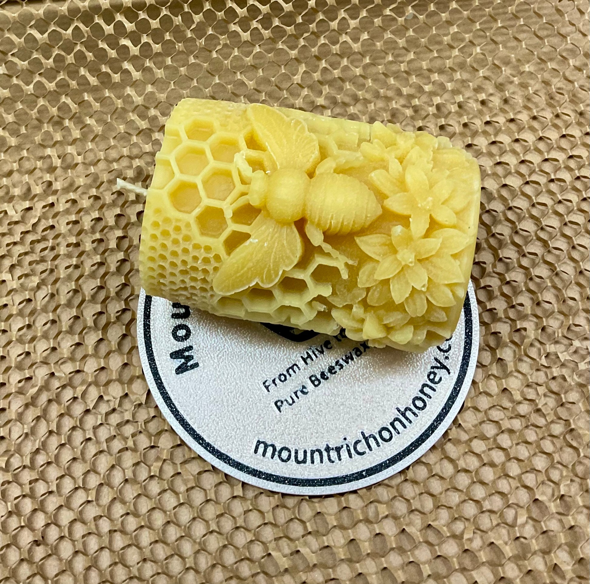 Beeswax candle with honeycomb design on a textured surface with a visible brand label.